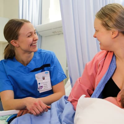 Mamma med bebis vid bröstet. Till höger om henne sitter en barnmorska.