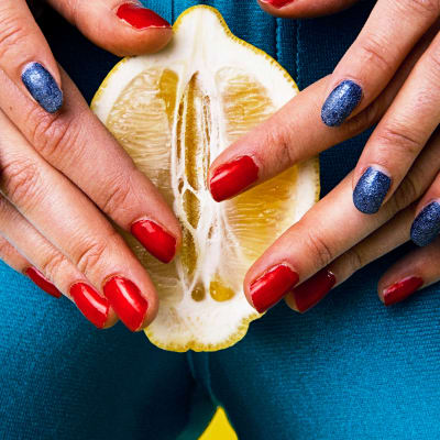 Kuvassa sitruuna, jota pitelee kahdet kädet, naisen haarojen välissä