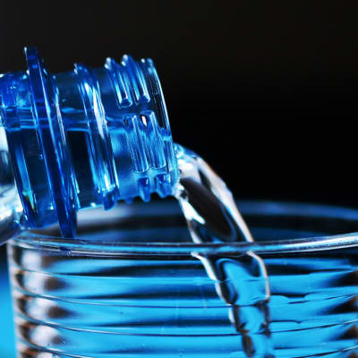 Vettä kaadetaan muovipullosta vesilasiin.
