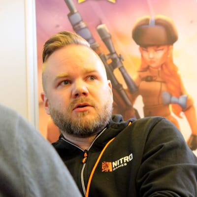 NitoGames pelifirman toimitusjohtaja Jussi Tähtinen istuu työpaikallaan, taustalla yrityksen roll-up