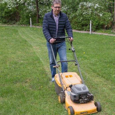 Mies leikkaa ruohonleikkurilla nurmikkoa.
