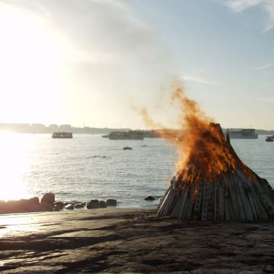 En midsommarbrasa som brinner på en strandklippa. 