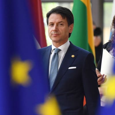 Italiens premiärminister Guiseppe Conte i bakgrunden, EU-flaggor i förgrunden.