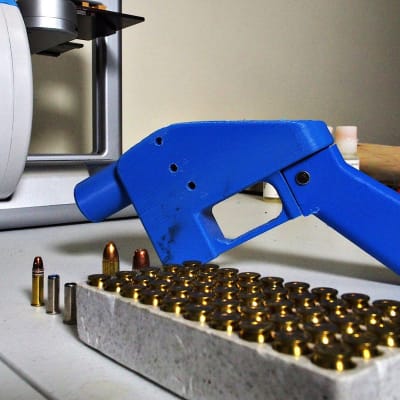 Kuvassa pistoolin edessä on 3D-tulostin, jolla pistoolin osat on valmistettu.