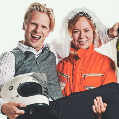 Joppe Dikert iklädd formulaoverall med sin man Oskar Pöysti i famnen. Han har en formel1- hjälm i famnen och en champagneflaska i handen. De ser ivriga och glada ut. 