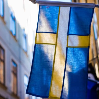 Ruotsin lippu, taustalla katunäkymää Tukholmasta.
