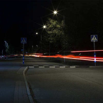 Pimeällä kadulla pitkällä valotusajalla otetussa valokuvassa auton valojen jättämät viirut.