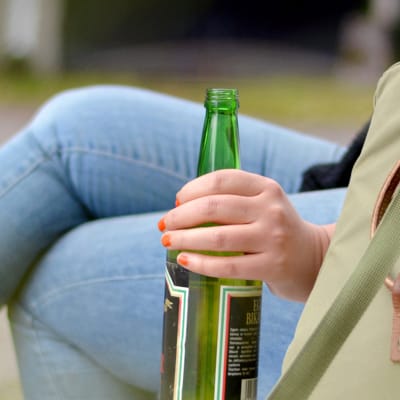 Nuori nainen istuu penkillä pullo kädessään.