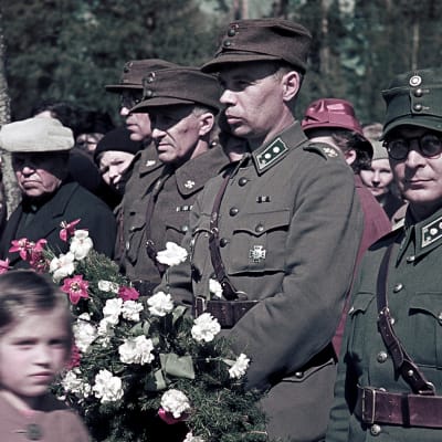 Sotilaita sankarihaudoilla kukkaseppeleet käsissään. 