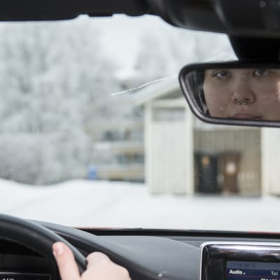 Nuori nainen ajaa autoa ja katsoo taakseen peilistä.