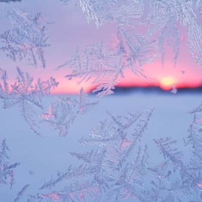 Jäähiutaleita ikkunassa ja takana auringonlasku.