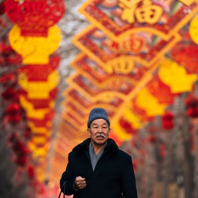 Kiinalainen mies kävelee punakeltaisten lyhtyjen alla jotka on ripustettu uuden vuoden juhlintaa varten.
