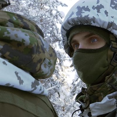 Varusmies pukeutunut kypärämyssyyn talvipakkasessa lumisessa metsässä