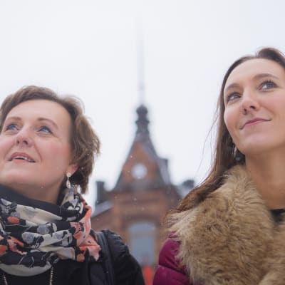 Pirjo ja Saija Viherlaakso seisovat ulkona, katsovat yläviistoon hymyillen.