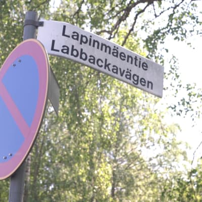 En trafikskylt med vägnamnet "Labbackavägen". I bakgrunden syns träd.
