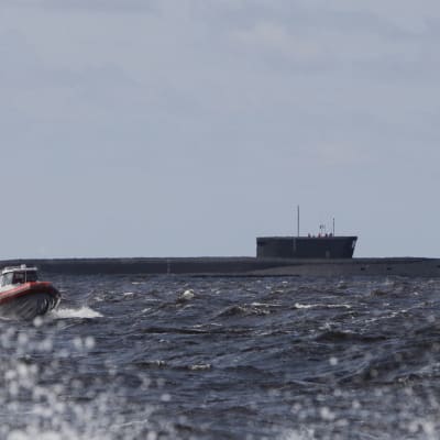 En ubåt ligger i vattnet. I förgrunden syns en motorbåt. Det är sjögång.