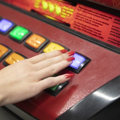 Rahapeliautomaatti lähikuvassa. Naisen käsi näppäimellä.