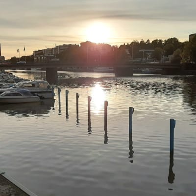 Solen går ner och speglas i Aura ås vatten i Åbo, där båtar ligger förtöjda i ån.