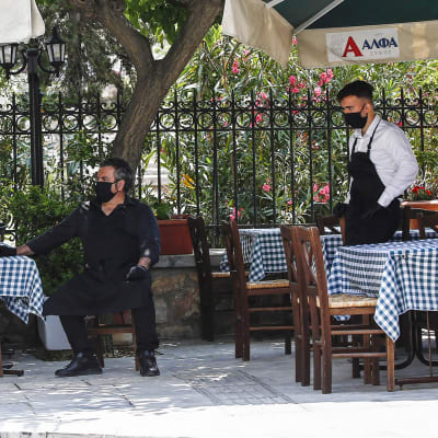 Ateenassa kasvomaskeihin suojautuneet tarjoilijat odottavat asiakkaita.