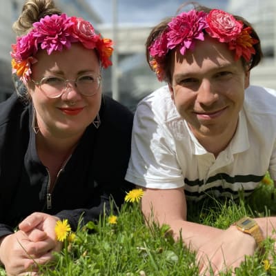 Programledarna för Hangö Teaterträff 2020 Kia Svaetichin och Tom Rejström ligger på gräsmattan med blommor i håret
