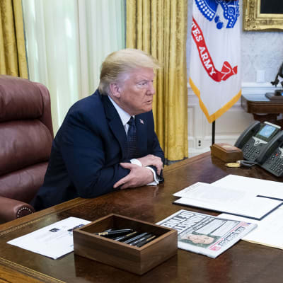 Dinald Trump istuu työpöydän ääressä.
