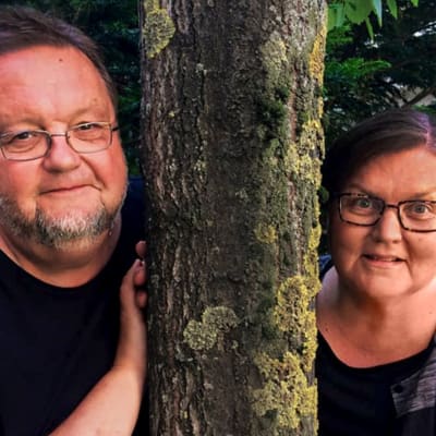 Toimittajat Risto Nordell ja Outi Paananen nojaavat puun runkoon ja katsovat kameraan.