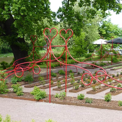 Röd skulptur av metall kring en trädgård.