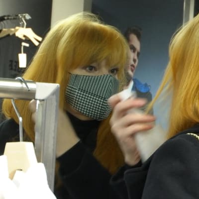 En kvinna med ansiktsmask speglar sig och rättar till håret. 