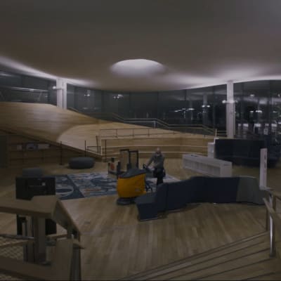 En bred bild inifrån biblioteket Ode på natten, lamporna lyser och en städare står mitt i bilden med en golvputsarmanick som han kör.