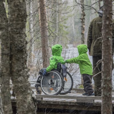 Lapsi työntää toista lasta pyörätuolissa esteettömällä retkeilyreitillä..