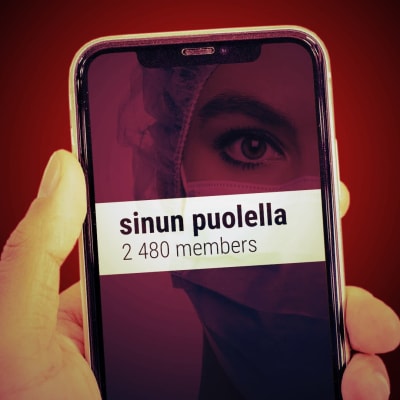 En hand håller i en telefonskärm. På skärmen syns en närbild av en kvinna i coronaskyddsutrustning. Tvärs över skärmen kan man läsa gruppnamnet "På din sida!" och "2480 medlemmar"