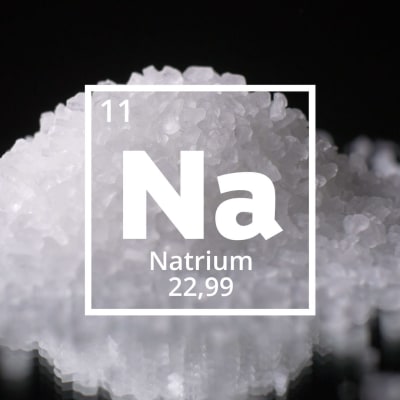 Natriums kemiska förkortning Na. I bakgrunden en hög med salt.
