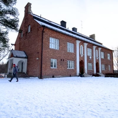En stor tegelbyggnad, med snöig gård. En person går framför byggnaden.