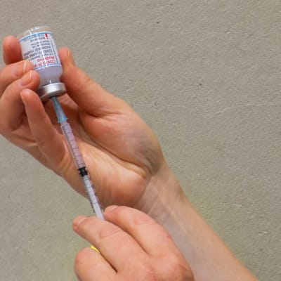Injektionsnål instucken i ampull med Modernas coronavaccin 