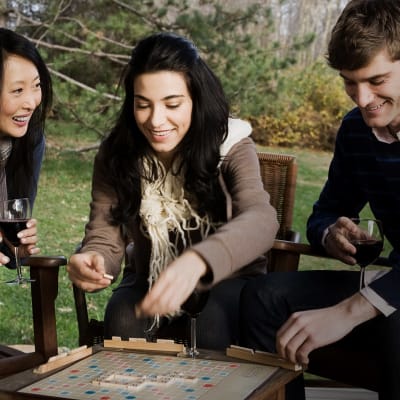 Kolme aikuista pelaa yhdessä Scrabblea terassilla.