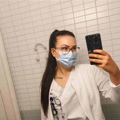 Selfie i en wc-spegel. Ronja Lindqvist iklädd munskydd och vita kläder. Hon studerar till sjukskötare.