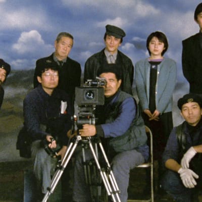 Kuvausryhmä poseeraa kameran takana, taustalla pilviä, kuva elokuvasta Elämän jälkeen, kuvassa myös teksti "Teeman elokuvafestivaali".