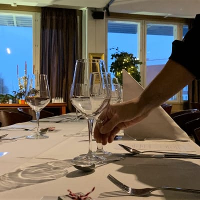 En hand arrangerar glasen på findukat restaurangbord med vita dukar.