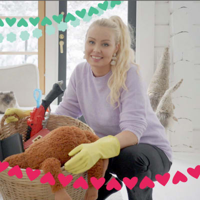Kuvassa siivousvaikuttaja Sonia Lindholm on kyykyssä ja pitelee käsissään pehmoleluilla ja muilla kodin tavaroilla täytettyä isoa koria.