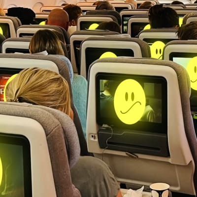 Ihmiset istuvat lentokoneessa ja katsovat näytöiltä hymynaamoja