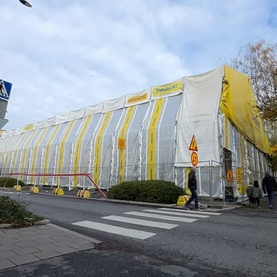 Ett våningshus intäckt i vit och gul plast på byggställningar. 