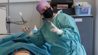 Annica Forsman, en kvinna klädd i sådana operationskläder som sjukskötare på op-avdelningen använder, står vid en brits där det ligger en docka. Dockan används i utbildning när man lär sig olika ingrepp under "operation".