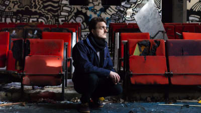 Viktor Granö på huk i ett utrymme med röda bänkar och graffiti samt skrot på marken