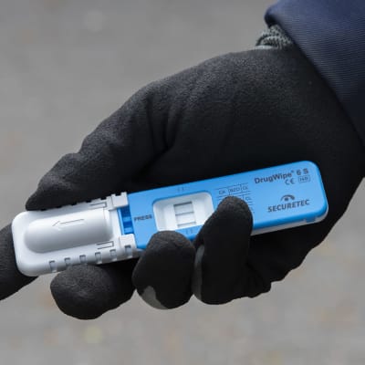 Poliisin sinivalkoinen huumetesteri kädessä, jossa on nahkahansikas. 