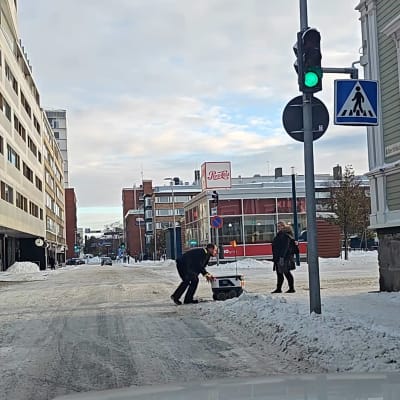 Mies työntää ruuankuljetusrobottia lumisessa Oulun keskustassa.