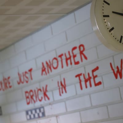 Koulun kello, seinässä teksti All in all you're just another brick in the wall