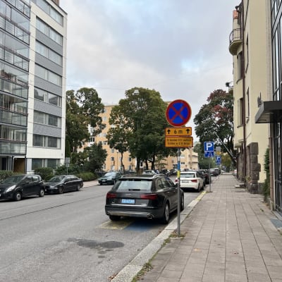 Bilar står parkerade vid en gata i Åbo. Närmast kameran finns en svart bil och en trafikskylt som förbjuder parkering förutom för bilar med CD-skylt.