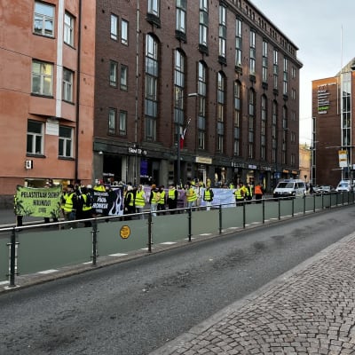 En grupp människor i reflexvästar går längs en gata, bär på banderoller.