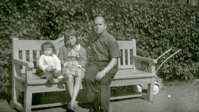 Anja Kauranen-Snellman taaperona, sisko-Maru ja isä-Ensio puistonpenkillä 1950-luvulla.