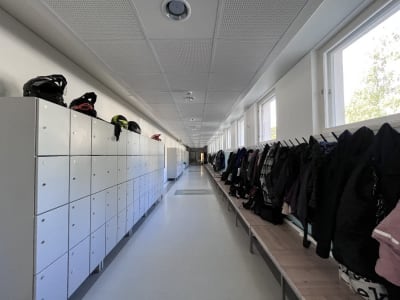 en lång skolkorridor med skåp på ena väggen och kapphängare på den andra